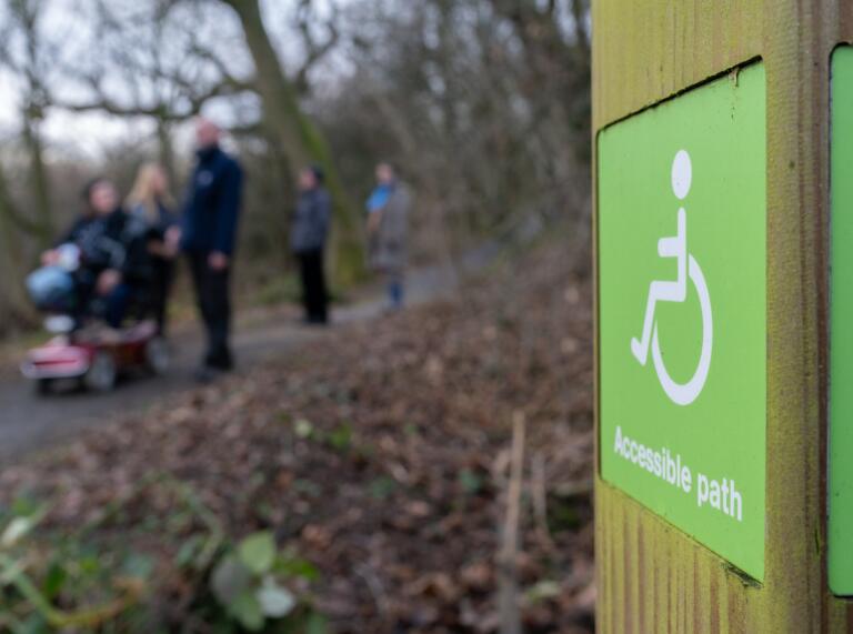 accessible path sign with group of people(blurred) including someone in a mobility scooter in background.