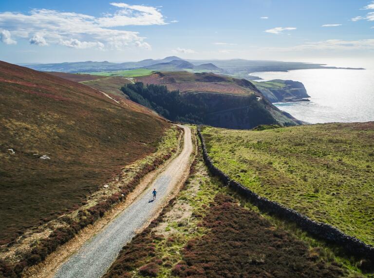 A narrow gravelled road with views over a rugged coastline.