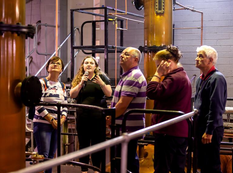 A group of people in a distillery looking at copper stills.
