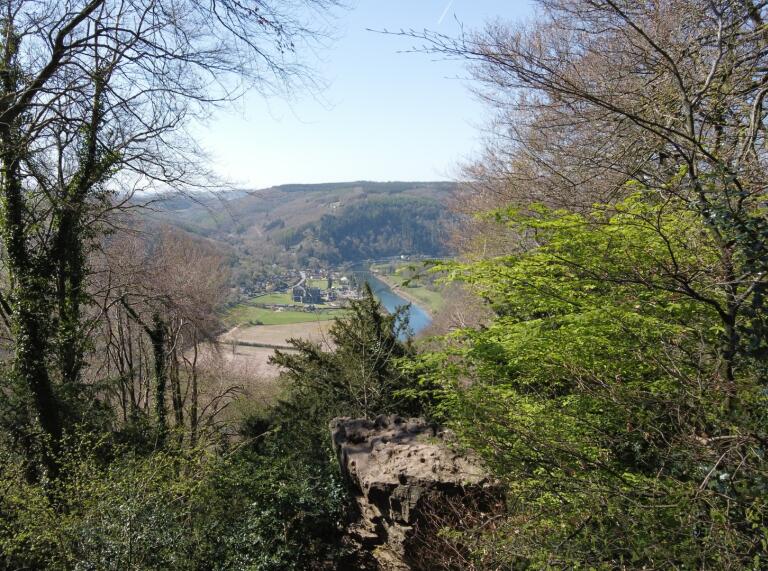 View from a hillside footpath down onto a valley with a ruined abbey next to a river. 