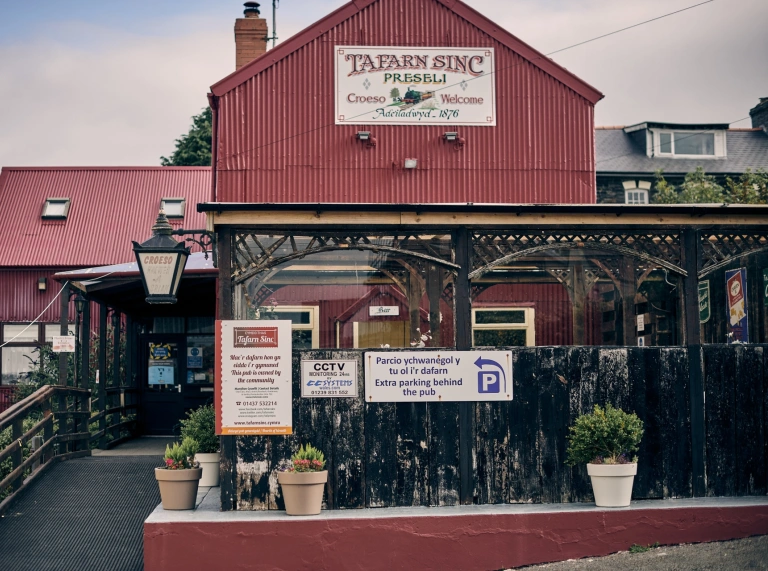 A red painted corrugated iron clad pub with a covered terrace outside.
