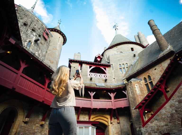 A woman taking a phone pic inside an ornate castle courtyard.
