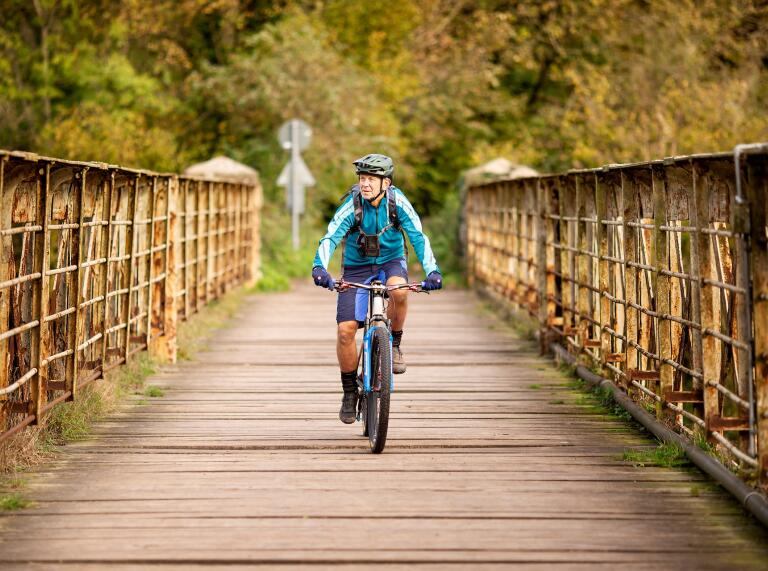 A man cycling over a wooden slatted metal sided bridge.