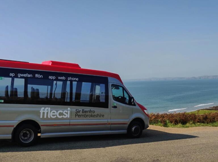 bus with the words fflecsi Sir Benfro Pembrokeshire on the side and sea in background