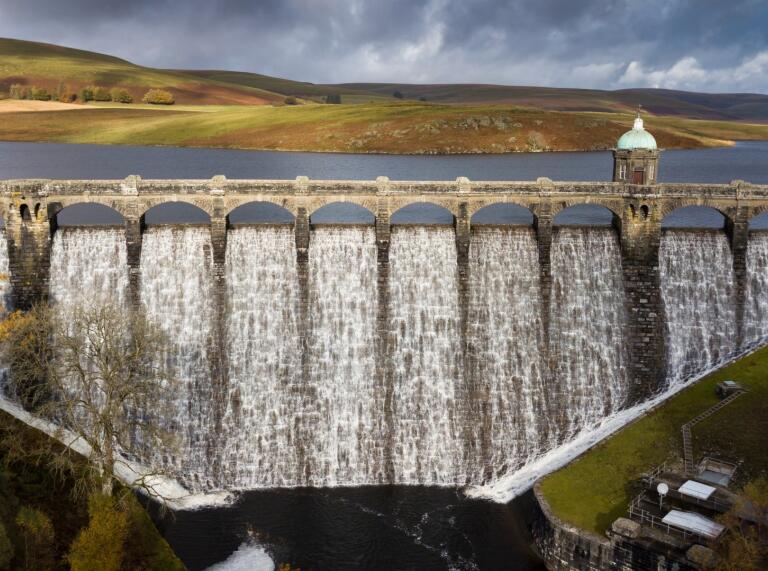 An ornate dam in the countryside, with water flowing over.