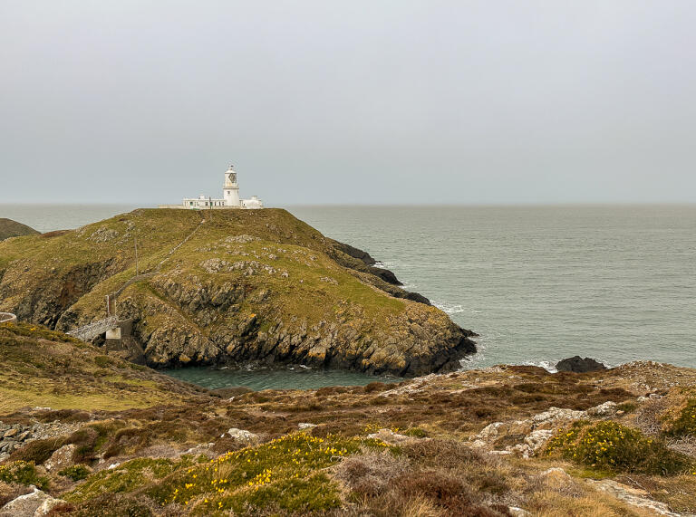 A white lighthouse tower on a rocky mound.