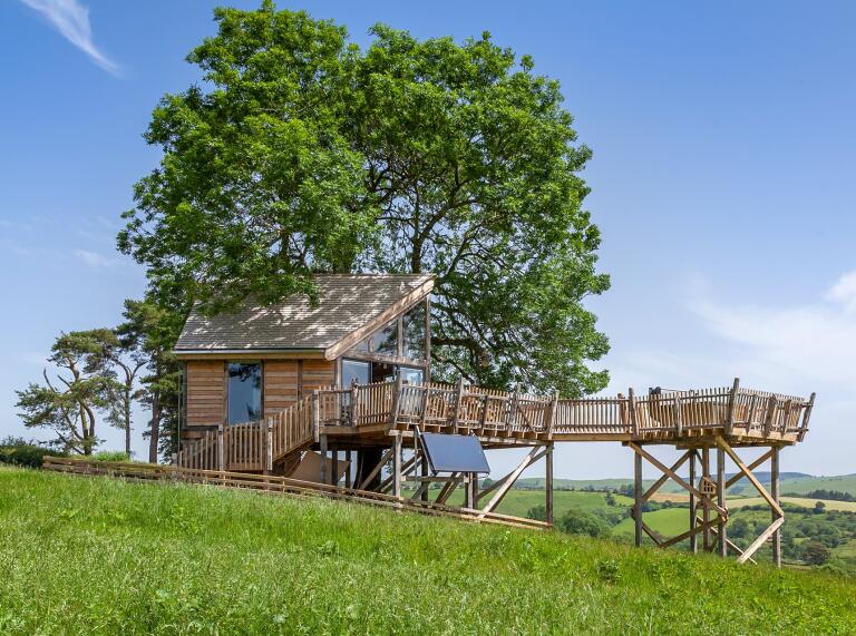 A treehouse surrounded by decking overlooking the countryside.
