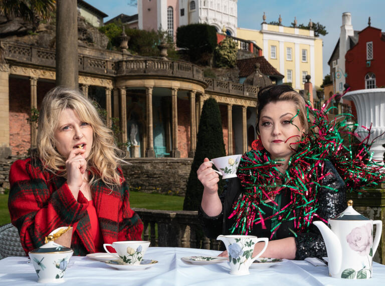 Two women having a cup of tea in ornate gardens.