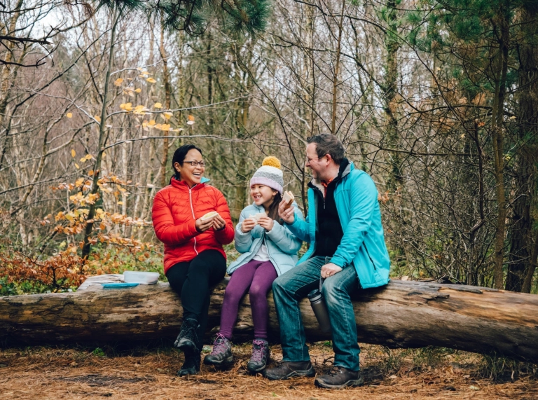 parents and daughter sat on log  in forest.