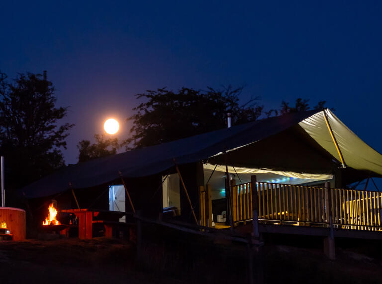A bright full moon over a safari tent with a wood fired hot tub on decking.
