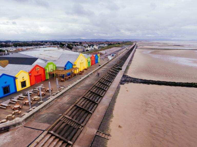 A sandy beach with a promenade and colourful huts on a dull day.
