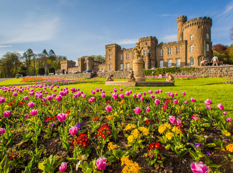 A Victorian castle with pink tulip beds in the foreground.