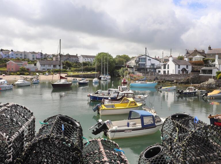 A small harbour with lobster pots, small fishing boats and a sandy beach.
