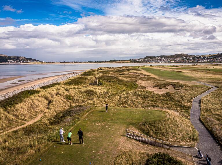 People playing on a coastal golf course with views over the sea and mountains.