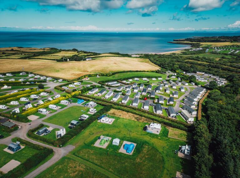 Campsite from above. Tents and caravans in fields near the coast . The sea can be seen in the distance