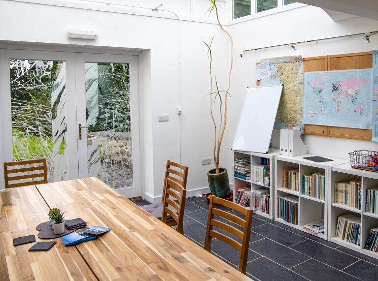 conservatory with a long wooden table and chairs and bookshelves.