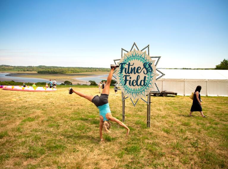 A woman doing a cartwheel by a sign 'fitness field'.