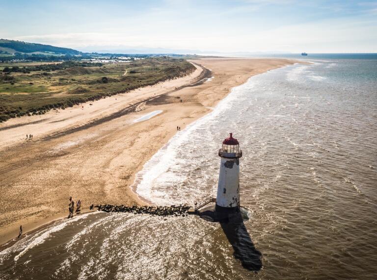 Aerial view of a lighthouse on a wide, sandy beach.
