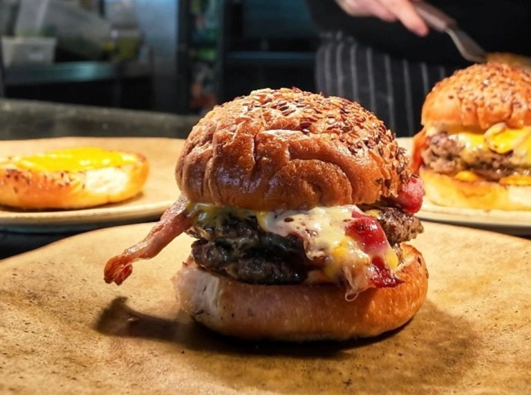 burgers on wooden platters with tattooed arm in background.