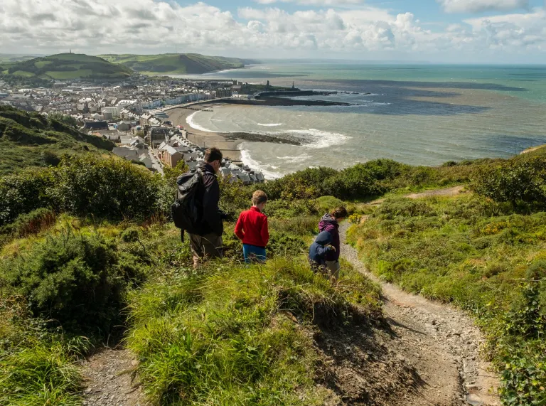 man and two children walking with view towards Aberystwyth coast.