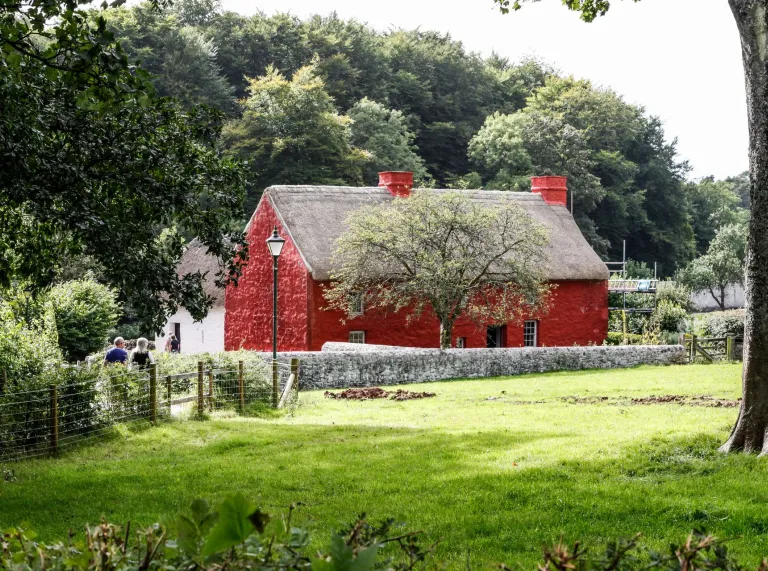 farmhouse building painted red with thatched roof in background with green field in foreground.