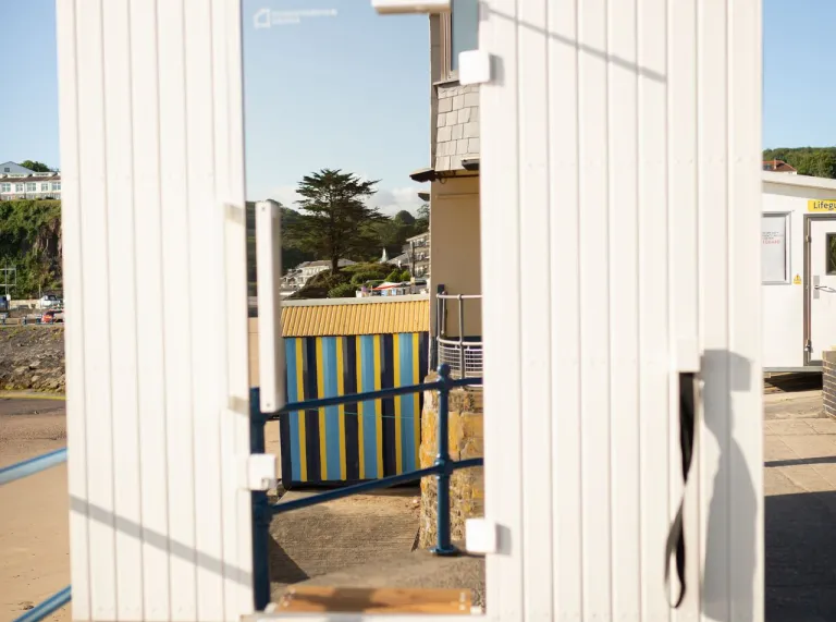 The exterior of a mobile sauna with white walls and wooden steps up to a mirrored door.