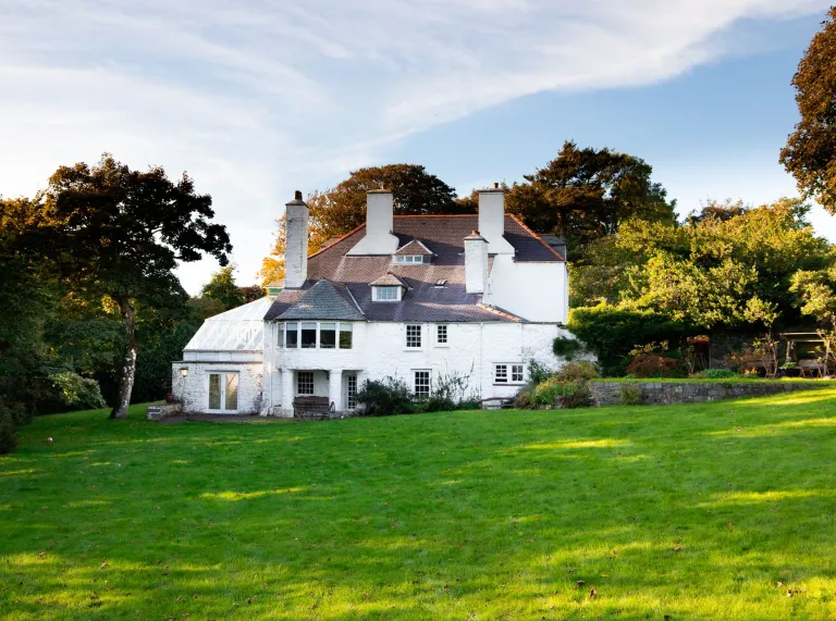 Die Rückseite eines großen, weißen Hauses mit grünem Rasen davor.