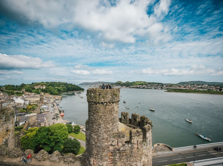 Turm einer Burg im Vordergrund mit eine Ort und einer Flussmündung und Booten dahinter.