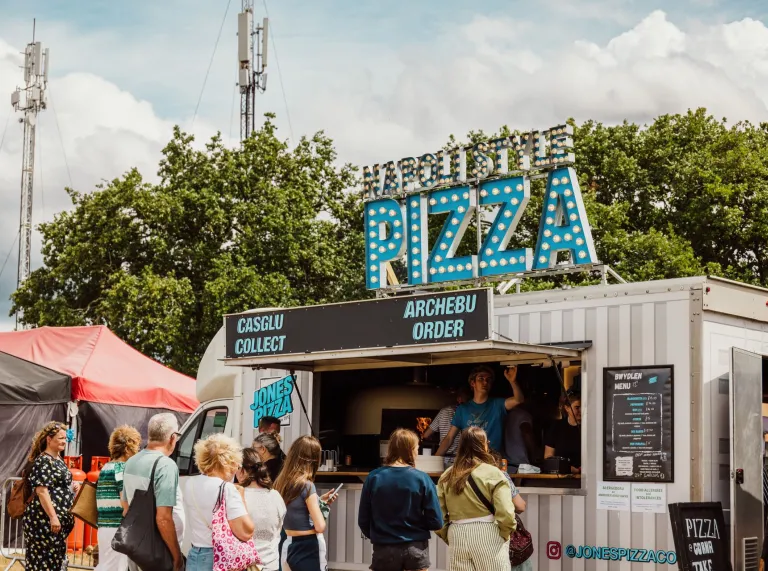 pizza food stall at National Eisteddfod with bilingual signage and people queuing.