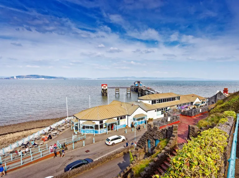A seaside village with a pebbly beach, pier and promenade.