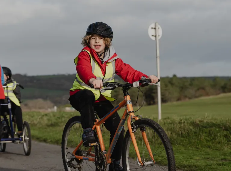 child wearing helmet on adaptive bike in country park.