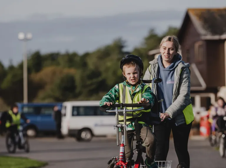 young child wearing helmet on adaptive bike being held by adult.