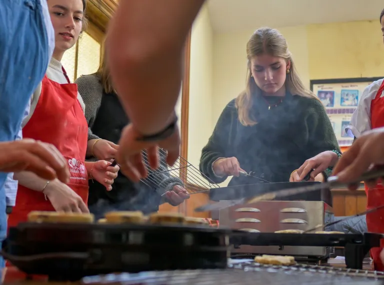 People wearing aprons cooking traditional Welsh dishes on a griddle during a St David’s Day celebration workshop.