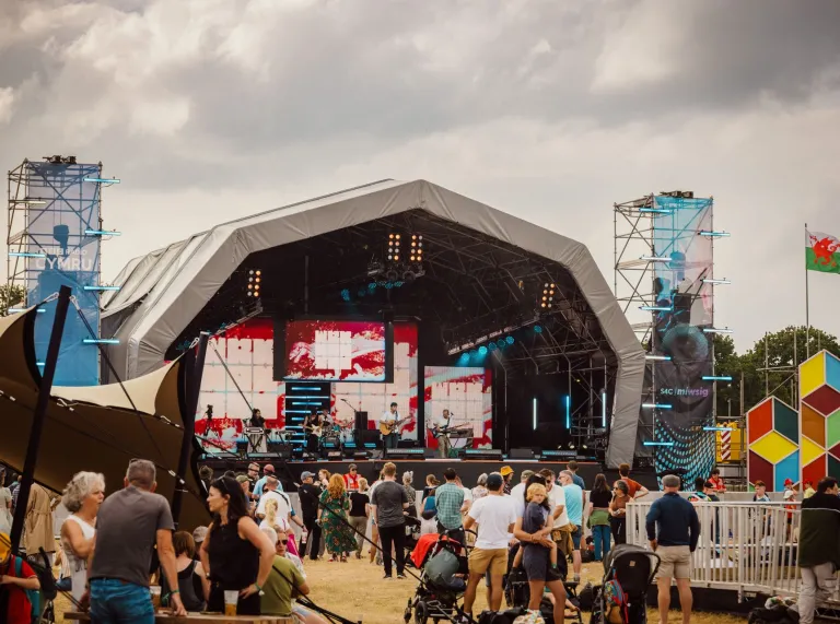 crowd enjoying Eisteddfod with stage and flags.