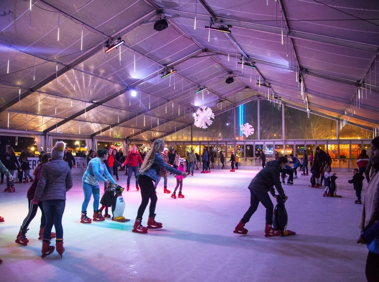 ice skaters in covered outdoor rink with coloured lights.