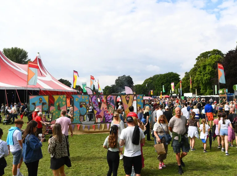 people walking at festival in park, with sign reading Tafwyl, tent and flags.