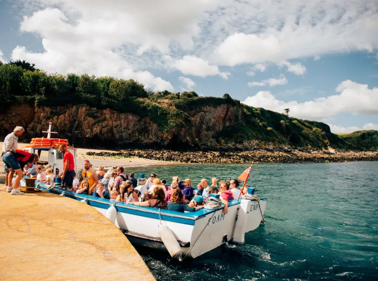 A small boat full of people, at a small harbour. 