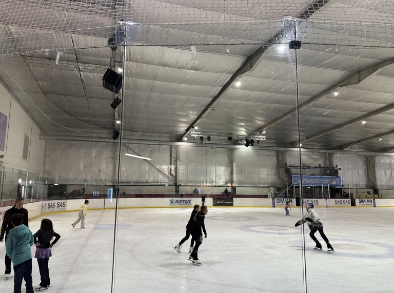 People skating inside an indoor ice rink.