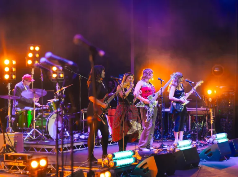 A band on stage singing and playing guitars, with a drummer at the back.