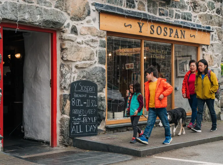 Two adults and two children walking past a cafe. 