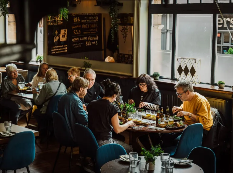 A group of people at a restaurant table trying different Welsh food and drink. 