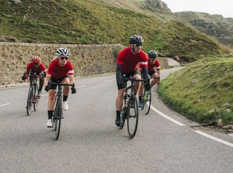 Eine Gruppe von vier Rennradfahrern in roten Jerseys mit Helm auf einer Straße in den Bergen.