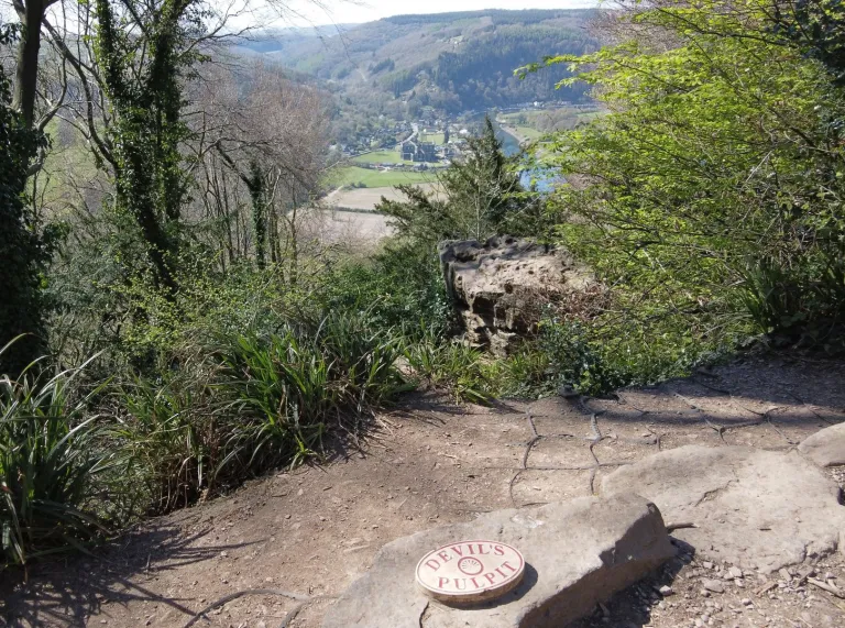 View of a ruined abbey across a river valley from a pathway.