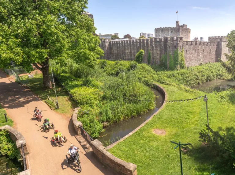 A group of cyclists using adapted bikes in a park with a castle. 