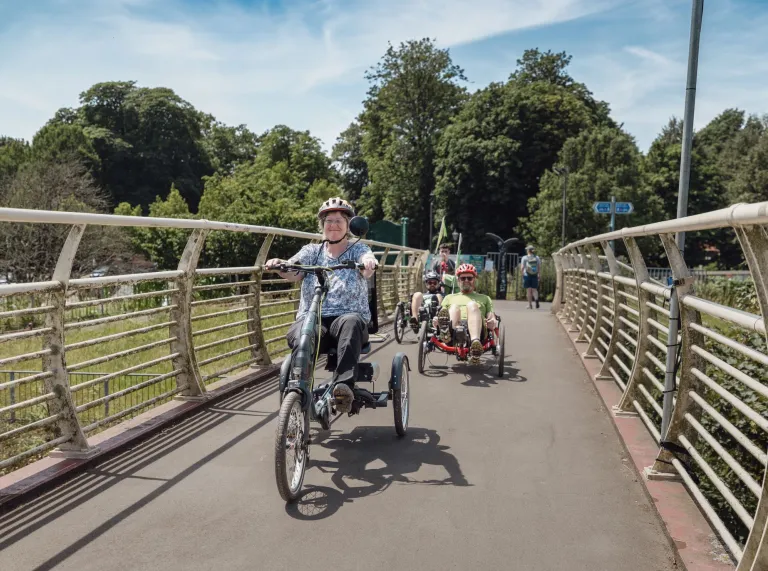 Cyclists riding over a river bridge path.