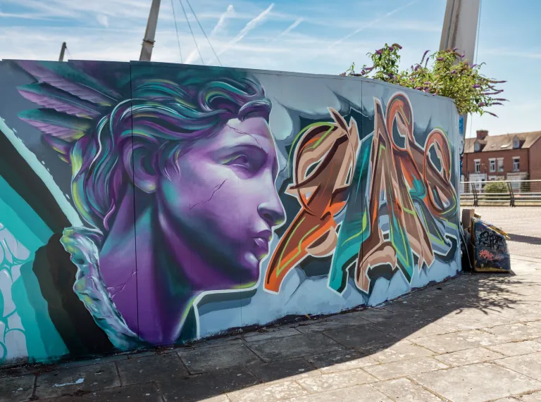 Large street art mural featuring a stylised purple classical statue and bold graffiti lettering on a wall near the Principality Stadium in Cardiff.