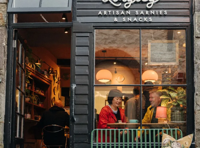 Exterior of Loafley café in Tenby, with customers seated inside by the window and a green bench outside.