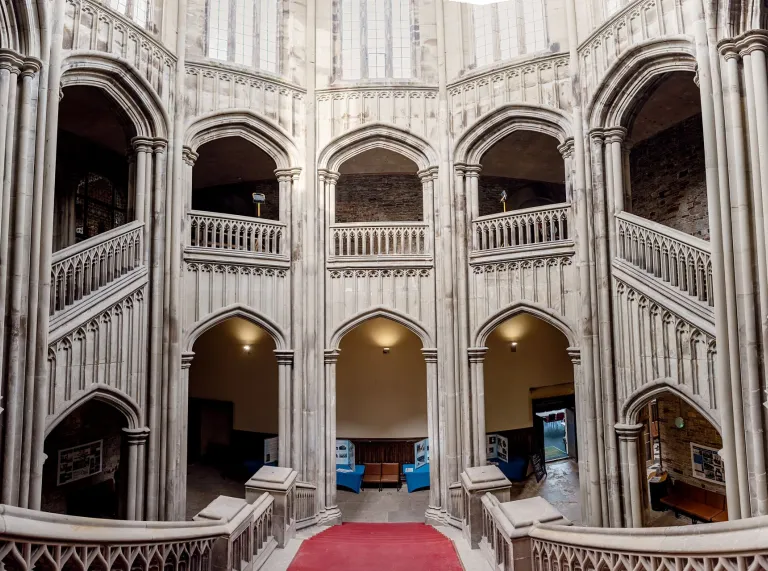 Grand stone staircase and Gothic arches inside Margam Castle's entrance hall, featuring ornate architectural details and a red carpeted stairway