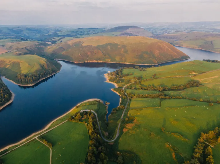 A reservoir from above, showing miles of green hills, and a twisty road following the lake side.