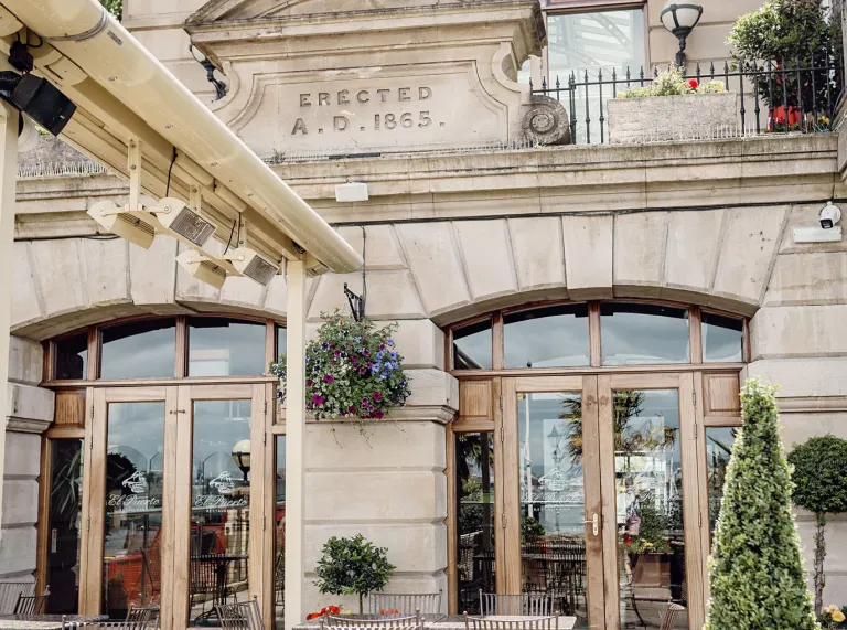 Outdoor restaurant terrace with tables and chairs outside a historic stone building.